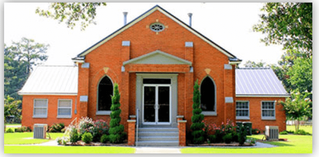 Brick building with arched windows and a gabled roof, surrounded by manicured landscaping, showcasing a welcoming entrance. Perfect for community events.