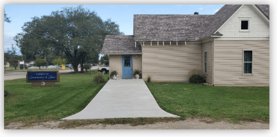 Community center with a blue door and landscaped pathway, surrounded by grass. A sign indicates "Community of Christ" nearby.