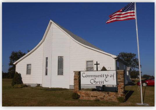 Community of Christ church building, featuring a prominent sign and flag, set against a clear blue sky. Represents local faith community.
