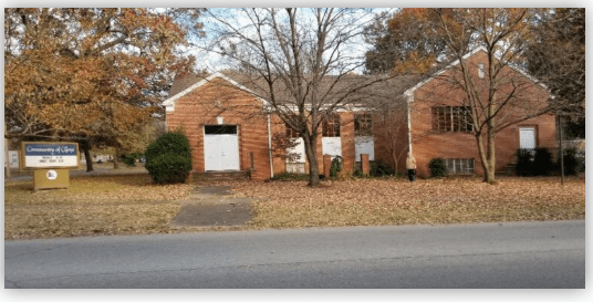 Brick building with a gabled roof and large front doors, surrounded by autumn trees and grass, housing the Community of Hope organization.